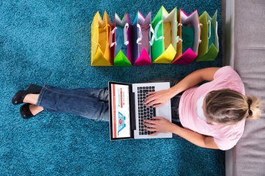 Yükseltilmiş bir kadın görünümünü halı üzerinde oturan ve Online alışveriş torbaları ile alışveriş