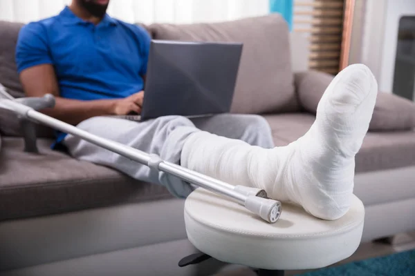 Mężczyzna Złamaną Nogą Siedząc Kanapie Przy Użyciu Laptopa — Zdjęcie stockowe
