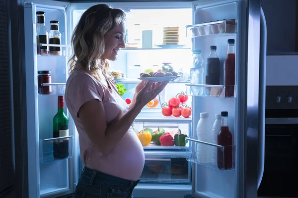 Молодая Счастливая Беременная Женщина Держит Тарелку Печенья Кухне Рядом Холодильником — стоковое фото