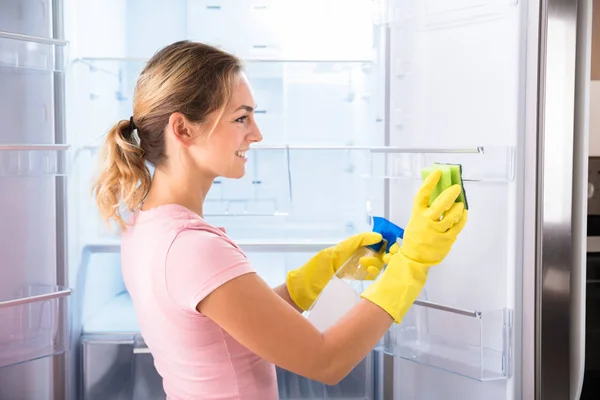 若い女性のスプレー ボトルとスポンジの冷蔵庫を掃除用手袋を着用 — ストック写真