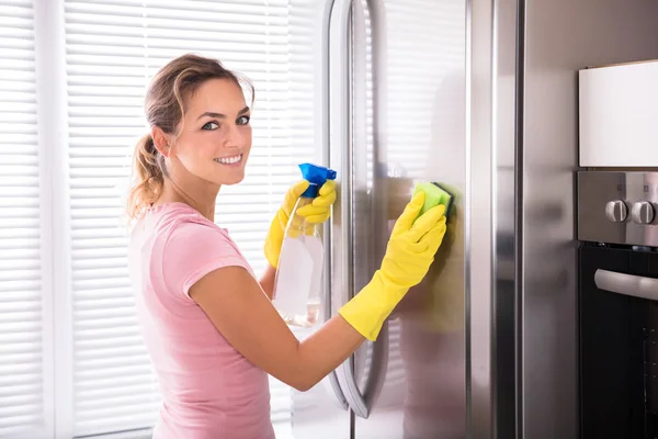 愉快的妇女清洗她的不锈钢冰箱用海绵和喷雾瓶 — 图库照片