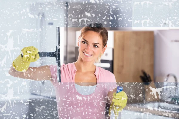 Young Happy Woman Wearing Yellow Gloves Cleaning Window With Squeegee And Spray Bottle