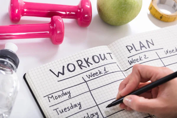 Woman Writing Workout Plan In Notebook At Wooden Desk