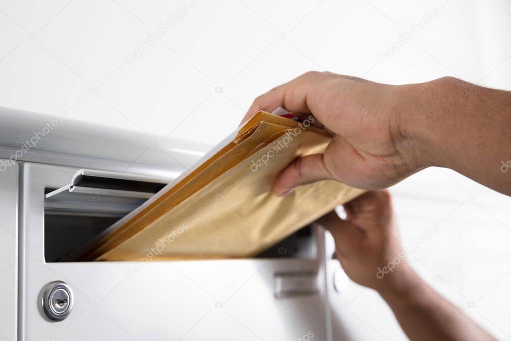 Close-up Of A Postman's Hand Putting Letters In Mailbox