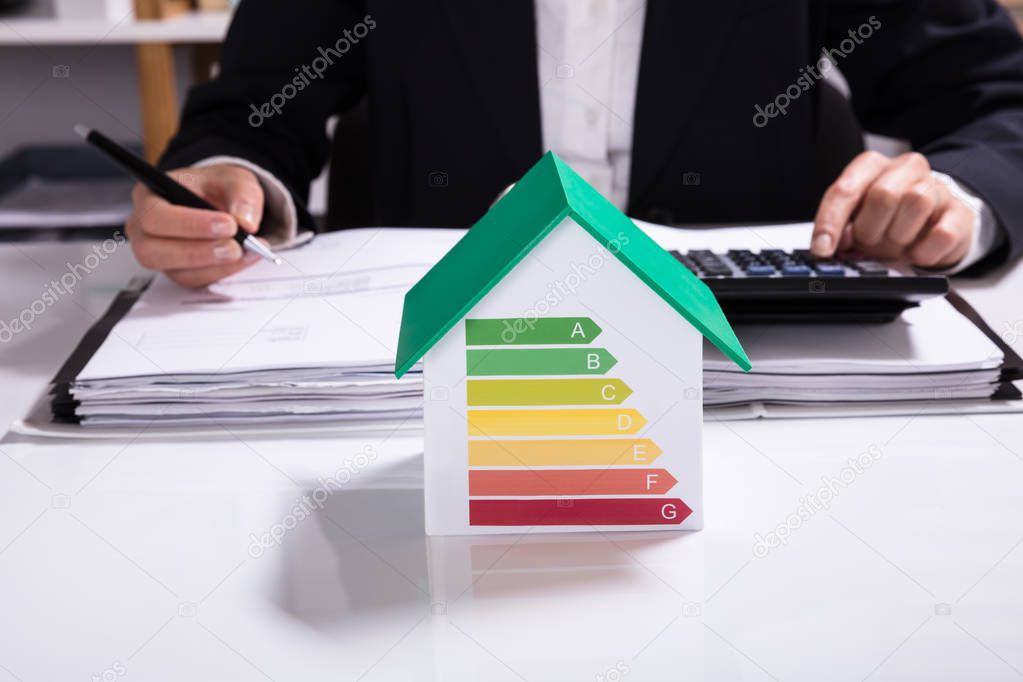 Businesswoman Calculating Financial Data With House Model Showing Energy Efficiency Rate On Desk