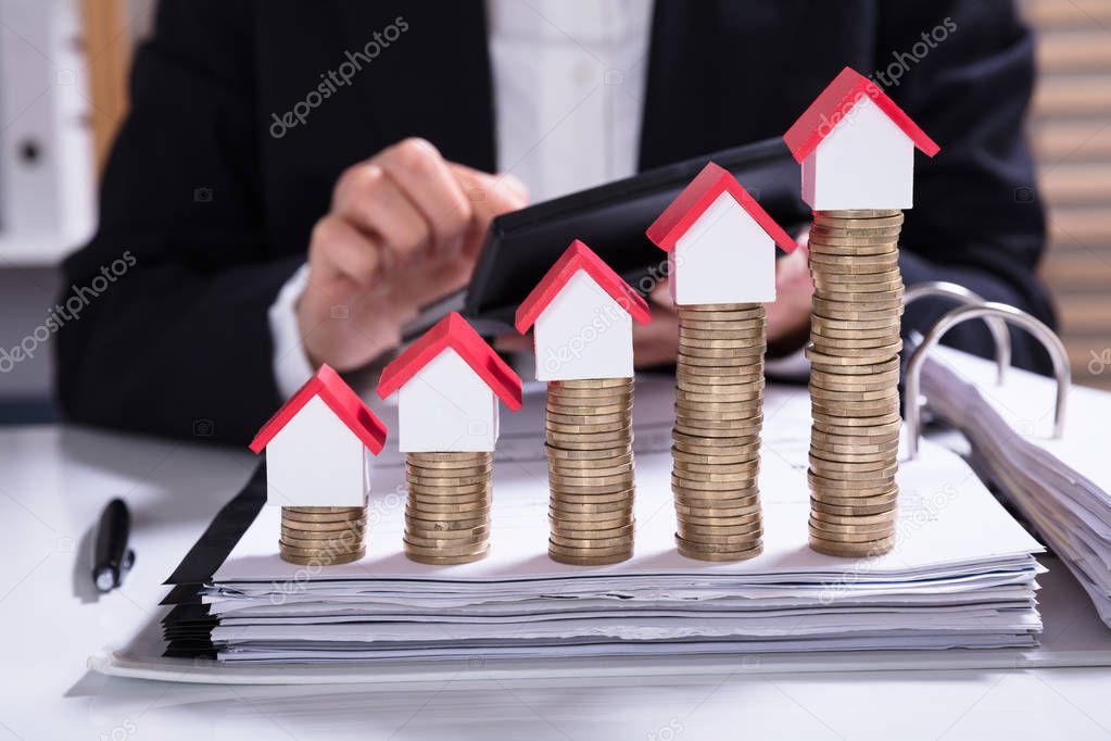 Midsection Of Businesswoman Calculating Invoice With House Models Arranged On Stacked Coins