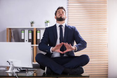 Ofiste Yoga yaparken masasında oturan genç işadamı