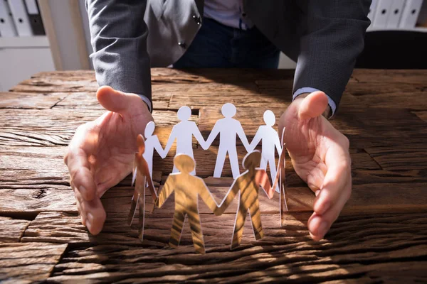 Businessperson Hand Protecting Paper Cut Out Figures Wooden Desk — Stock Photo, Image