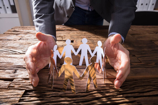 Рука предпринимателя защищает бумагу вырезанные фигурки на деревянном столе
