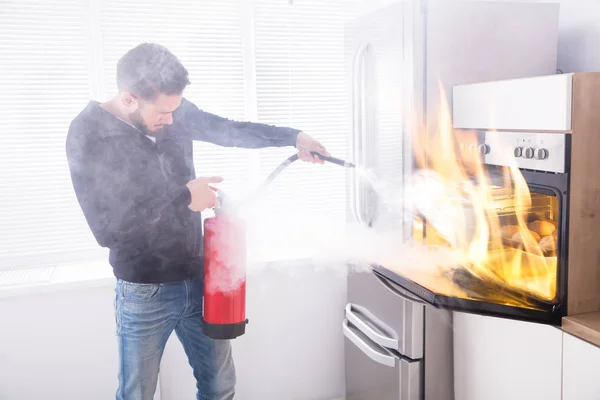 Young Man Using Red Fire Extinguisher Stop Fire Coming Oven — Stock Photo, Image