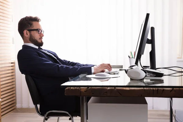 Man Sitting In Bad Posture Working On Computer In Office