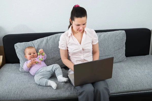 Mulher Sentada Sofá Usando Laptop Enquanto Seu Bebê Brincando Com — Fotografia de Stock