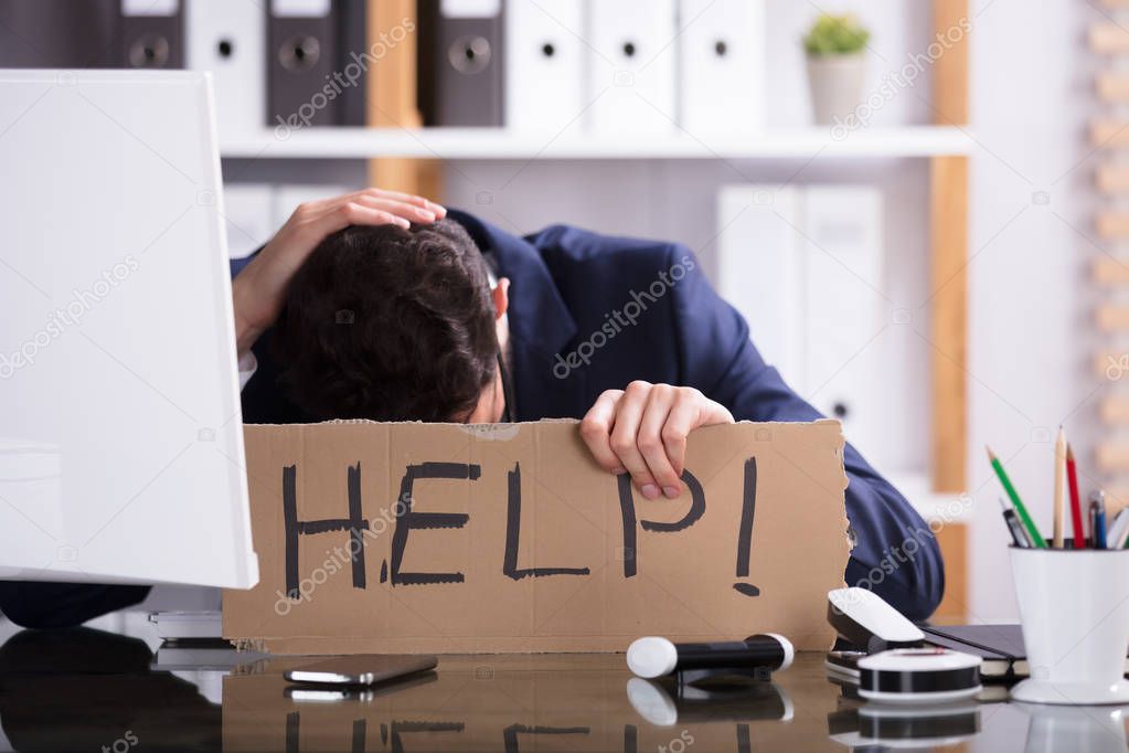 Young Businessman Holding Cardboard With Help Text At Workplace