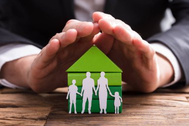 Ahşap masanın üzerinde işadamı'nın el ev modeli ve aile kağıt koruma kes şunu