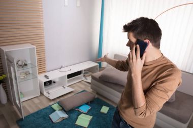 Genç adam konuşurken endişeli telefon ve çalıntı televizyona işaret ayarla evde