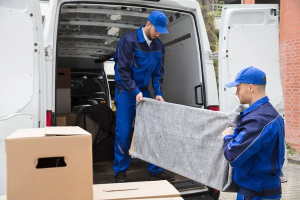 两名年轻男性工人穿着蓝色制服从卡车上卸下家具 — 图库照片