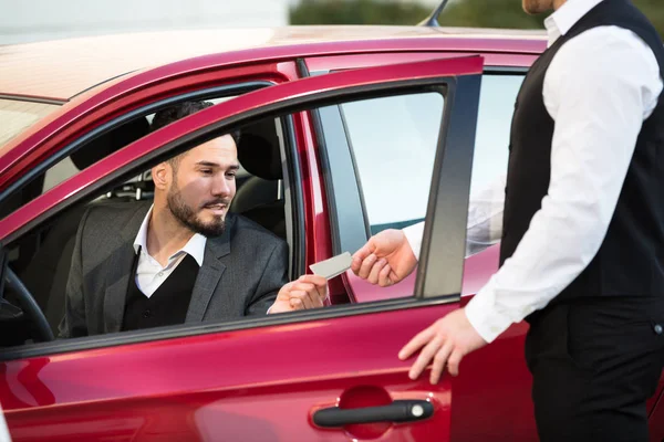 赤い車の中に座って若い男性ビジネスマンに与えているレシートを係員します — ストック写真