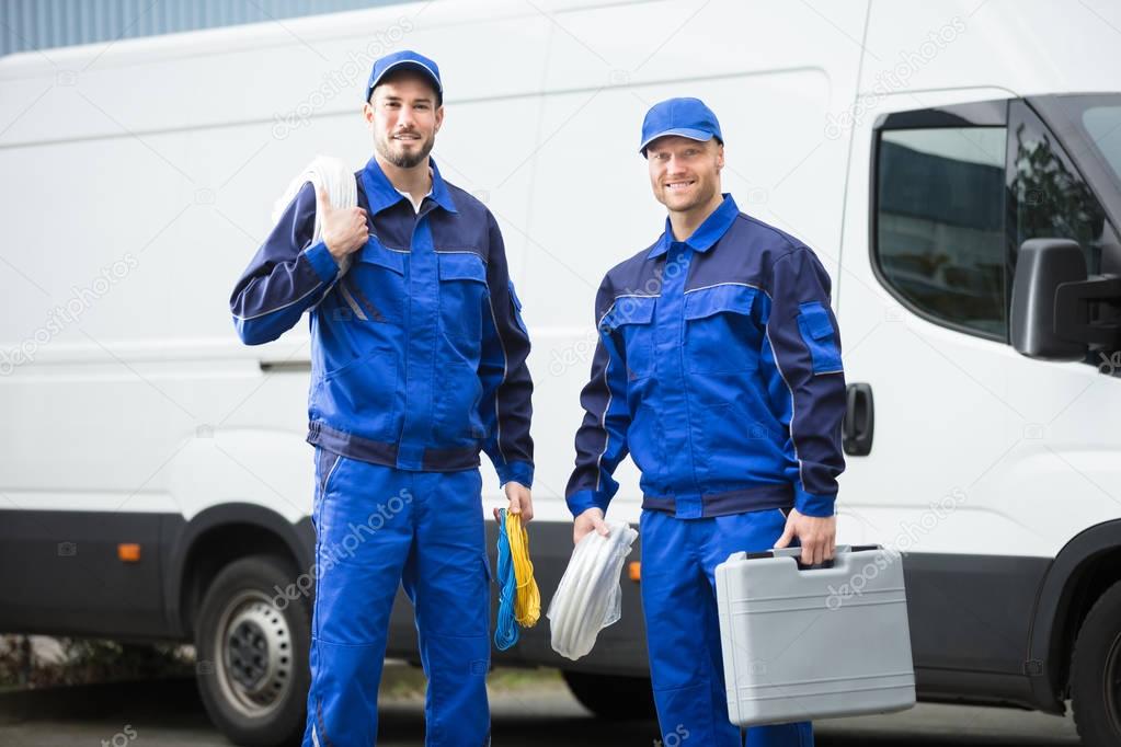 Smiling Repairman With Toolbox And Cable Standing In Front Of Vehicle