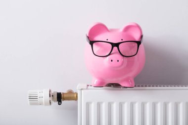 Termostat ve radyatör beyaz duvara gözlük ile Piggy banka Close-Up