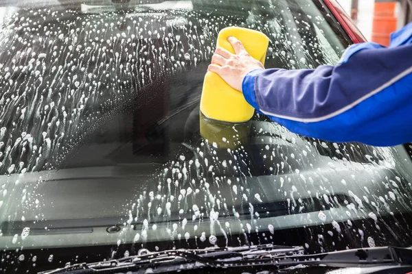 Person's Hand Cleaning Car Windshield With Sponge At Service Station