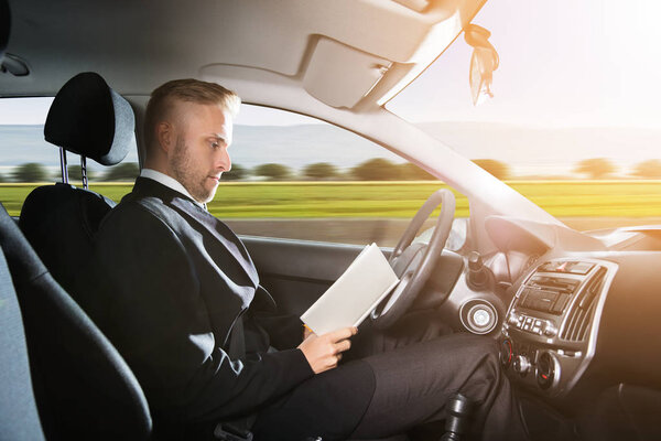Young Businessman Sitting Inside Self Driving Car And Reading Book