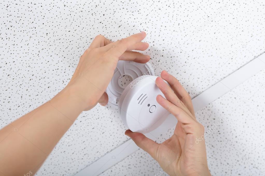 Low Angle View Of A Person's Hand Installing Smoke Detector On Ceiling Wall At Home