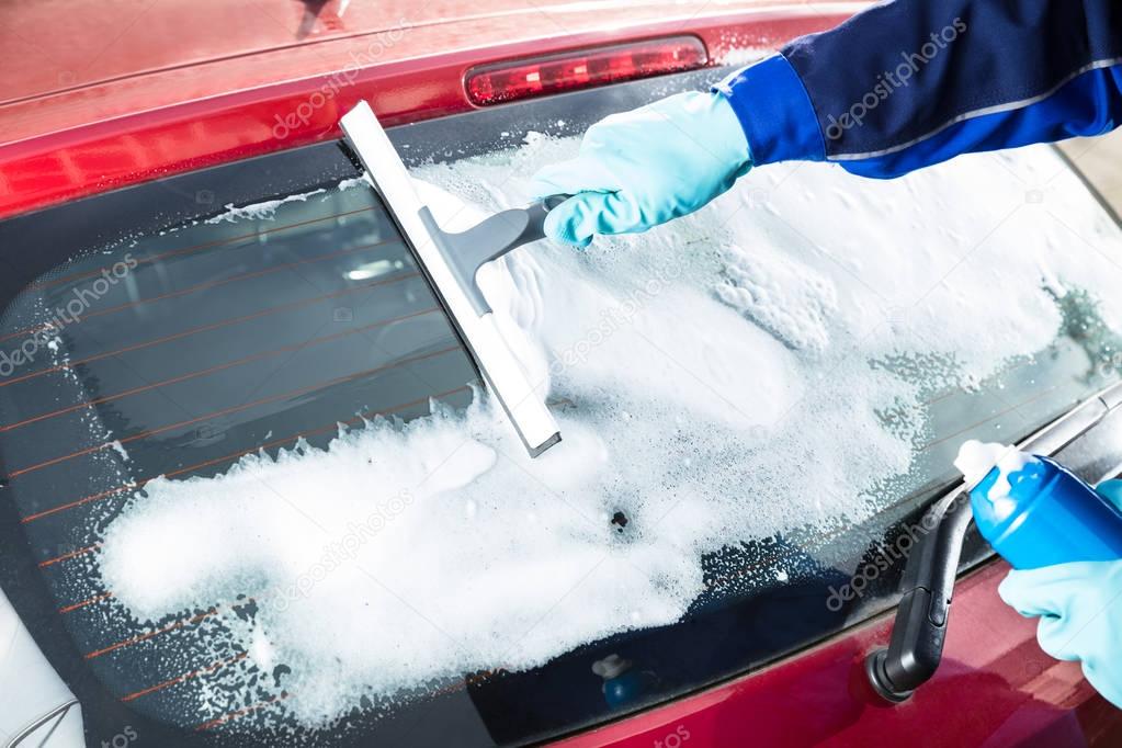 Close-up Of Person's Hand Washing Rear Windshield Of A Car Using Squeegee