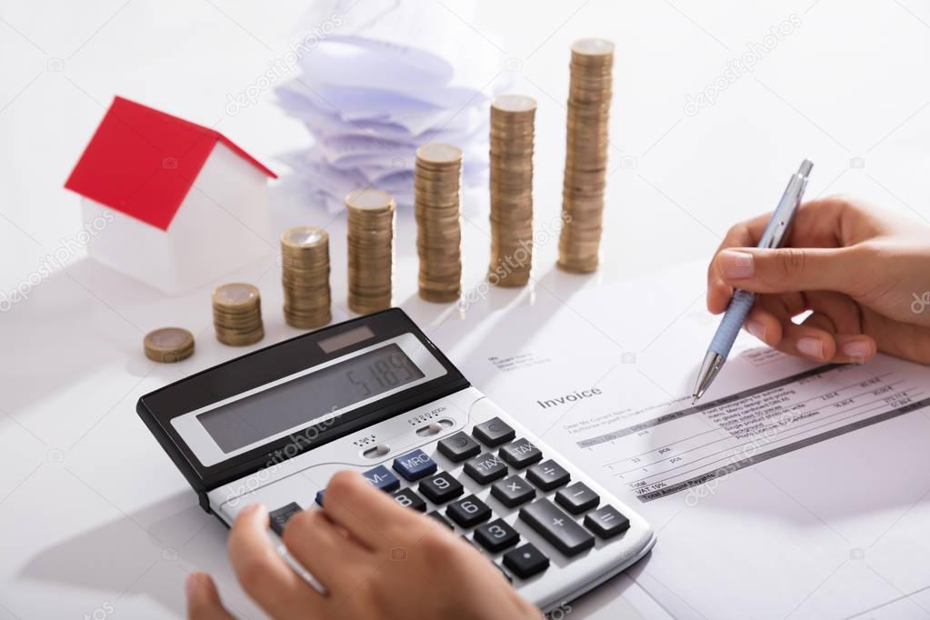 Businessperson Calculating Invoice With Stacked Of Coins In Office