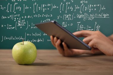 Yakın çekim yeşil elma üstünde okul sırası ile dijital Tablet kullanarak bir öğrencinin el