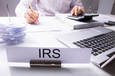 IRS tabela önünde muhasebeci hesap makinesi ve Laptop ile masa üzerinde vergi hesaplama