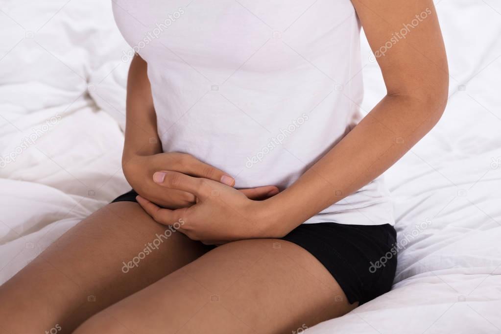 Mid Section View Of Woman Suffering From Stomach Pain Sitting On Bed