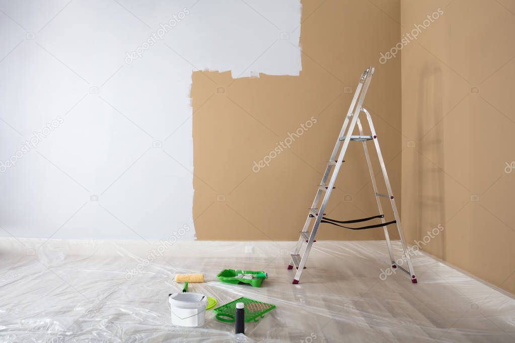 Half Painted White Wall With Ladder And Painting Equipments At Home