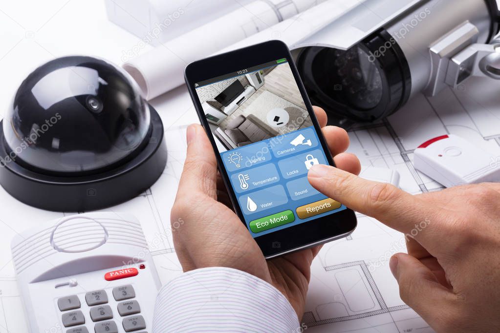 Person Hand Using Home Security System On Mobilephone With On Blueprint With Security Equipment