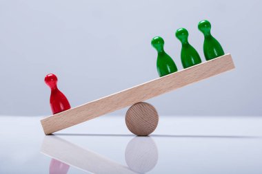 Red And Green Pawns Figures Balancing On Wooden Seesaw Over The Desk clipart