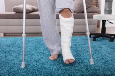 Kırık bacak mavi halı üzerinde yürümek için koltuk değneği kullanarak adamla