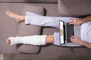 Dizüstü bilgisayarda bir adamın doktor ile sıvalı bacak Video konferans ile yüksek açılı görünüş