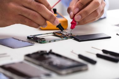 Hareket eden telefon ile masa üzerinde dijital multimetre inceleyerek bir teknisyen el Close-Up