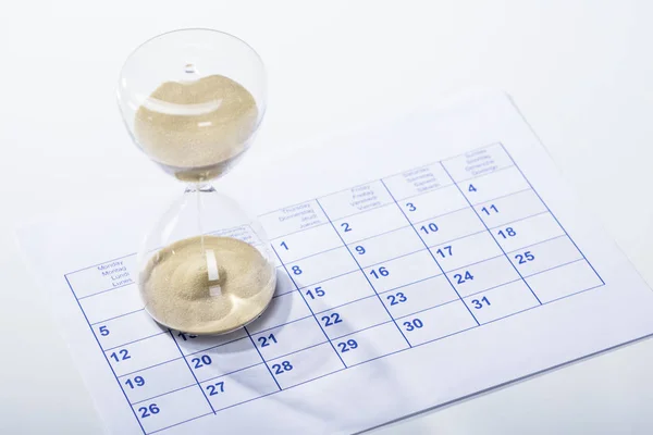Elevated View Of Hourglass On The Calendar Sheet Against The White Background
