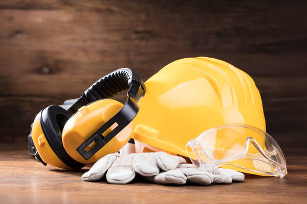Close-up Of Ear Muff, Safety Glasses, And White Gloves On The Wooden Table