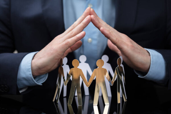 Крупный план руки бизнесмена, защищающего бумагу, вырезающего людей на столе
