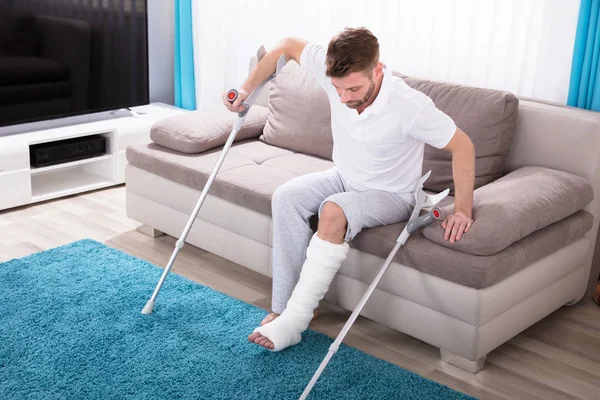 Junger Mann Mit Gebrochenem Bein Mit Krücken Vom Sofa Aufstehen — Stockfoto