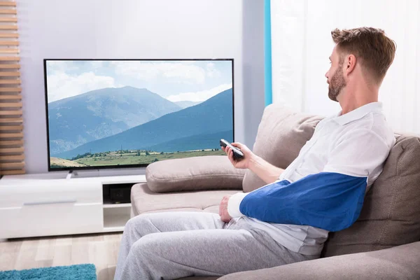 Joven Con Mano Fracturada Sentado Sofá Viendo Televisión Casa —  Fotos de Stock