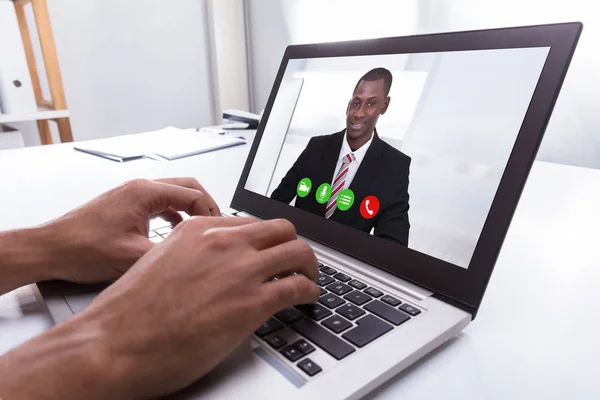 Close-up Of A Businessperson\'s Hand Video Conferencing With Male Colleague On Laptop At Workplace