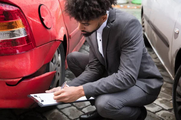 Jovem Agente Seguros Masculino Escrevendo Área Transferência Enquanto Examina Carro — Fotografia de Stock