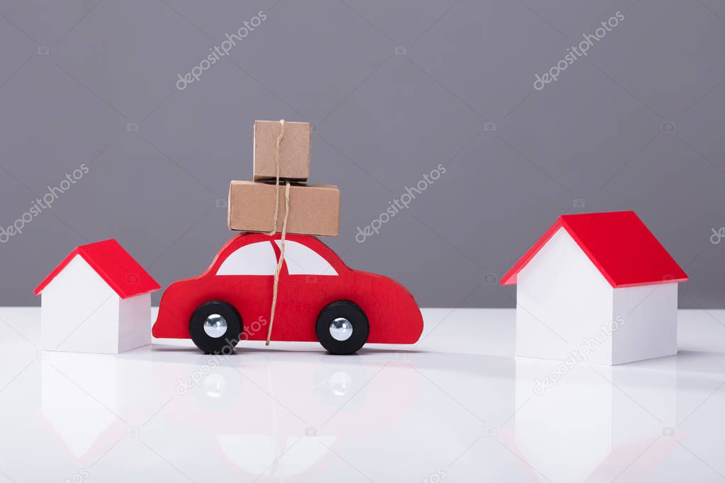 Red Car Transporting Cardboard Boxes From One House To Another On White Desk