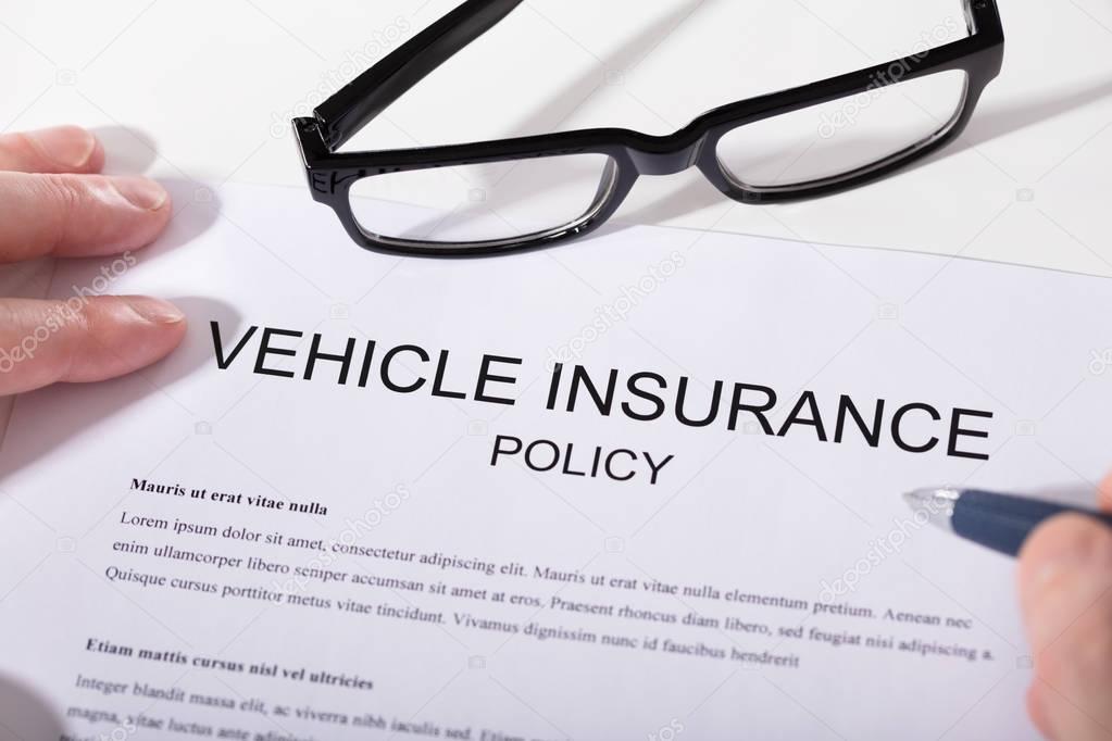 Elevated View Of Person's Hand Holding Pen Over Vehicle Insurance Policy Form