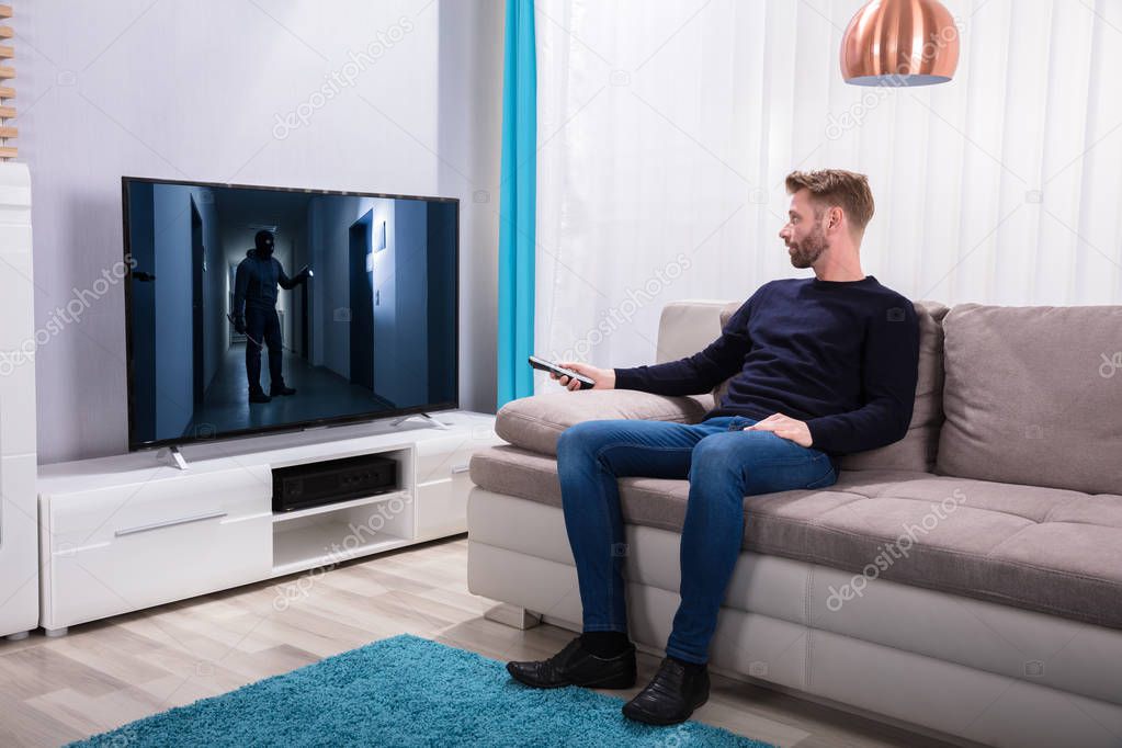 Young Man Sitting On Sofa Watching Suspense Movie On Television