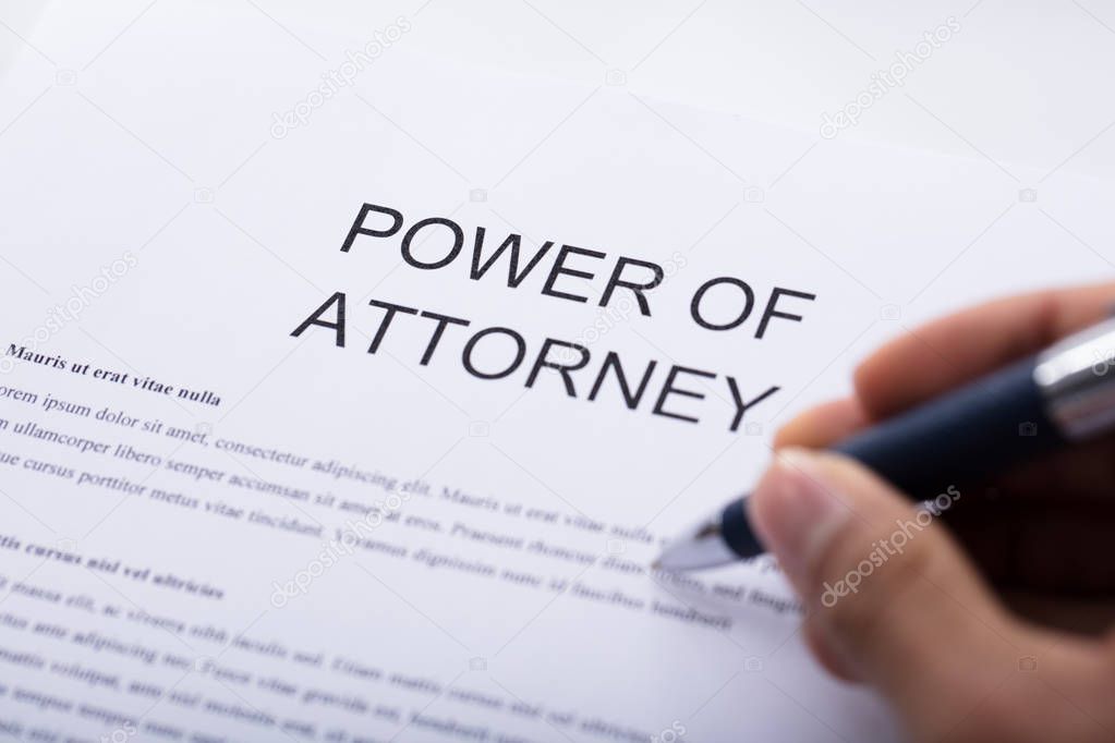 Close-up Of A Person's Hand Filling Power Of Attorney Form
