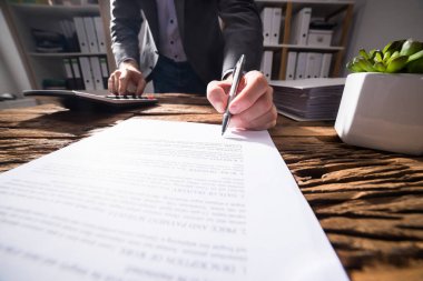 Ahşap masa üzerinde belge imzalarken hesap makinesini kullanarak bir işadamının'ın el Close-Up