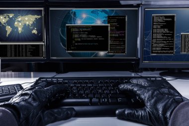 Birden çok bilgisayar önünde klavye kodu yazarak eldiven giymiş hacker